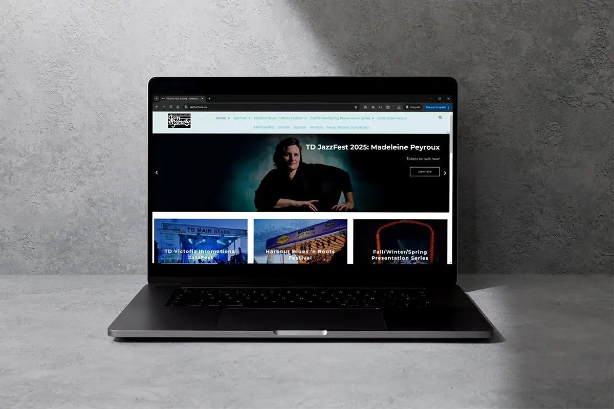Laptop on gray surface showing a jazz festival website with a header of a person.